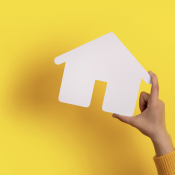 Hand holding white paper house in front of yellow background