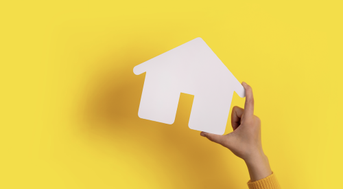 Hand holding white paper house in front of yellow background