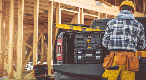 Construction worker standing by work truck with framed house in the background