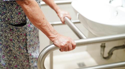 Old woman holding handrail next to bathroom sink