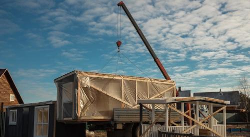 Crane lowering prefabricated house panel onto jobsite for affordable homes