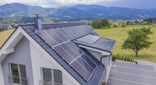 Solar panels on roof of gray house surrounded by fields and mountains